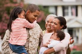 A man in fatigues holding two children and hugging an older woman.