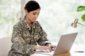 A woman in camouflage uniform using her laptop.